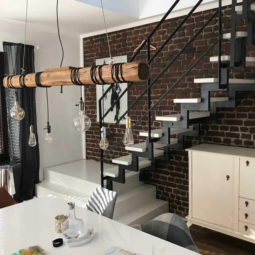 Wohnzimmer mit offener Treppe mit weißen Stufen und dunklem Geländer vor weißem Esstisch unter Holzlampe