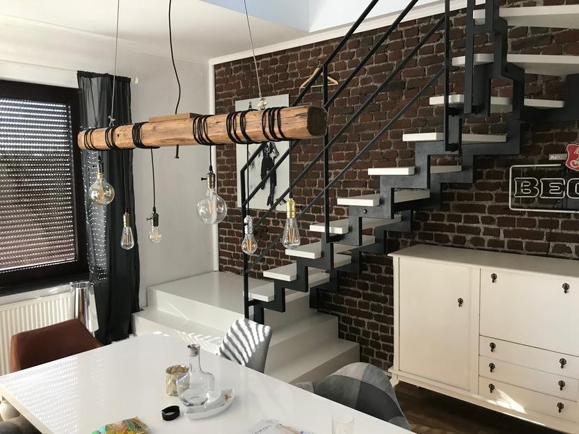 Wohnzimmer mit offener Treppe mit weißen Stufen und dunklem Geländer vor weißem Esstisch unter Holzlampe