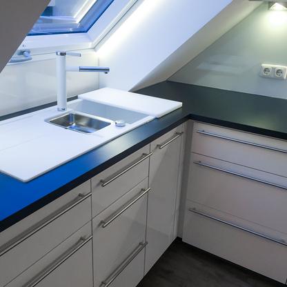 Küche unter Dachschräge mit weißen Fronten und dunkler Arbeitsfläche