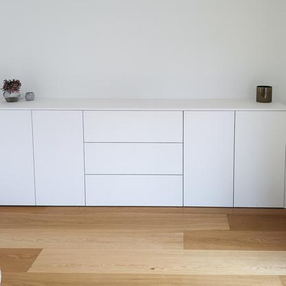 Schlichtes, weißes Sideboard mit dekorativen Elementen an einer Wand auf Holzboden.
