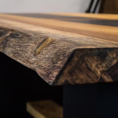 Nahaufnahme der Ecke eines Holztisches mit natürlicher Maserung und einem schwarzen Mittelstreifen.