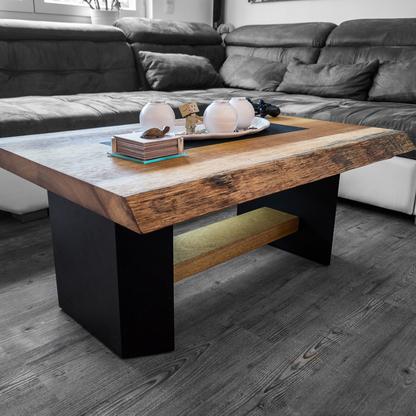 Ein Couchtisch aus Holz mit schwarzem Akzent, Büchern und Deko in einem gemütlichen Wohnzimmer.