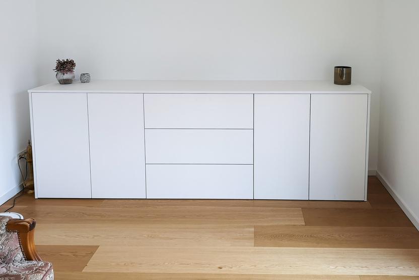 Minimalistisches weißes Sideboard im modernen Wohnzimmer. Schlichtes, weißes Sideboard mit dekorativen Elementen an einer Wand auf Holzboden.