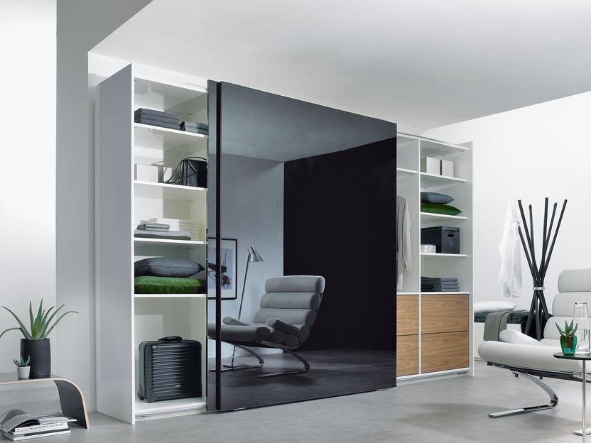Wohnraumimpression mit abgetrennter Ruheoase Wohnraumimpression mit abgetrennter dunkler Glasschiebetür für Ruheoase und integrierten Einbauregalen